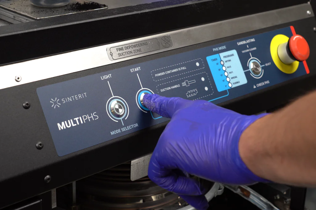 Close-up of a gloved hand pressing the start button on the Sinterit MULTIPHS powder handling system.